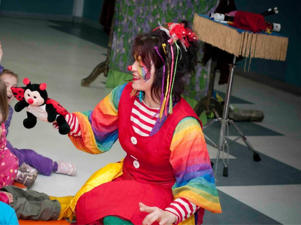 Femme déguisé en clown jouant avec des peluches avec des enfants