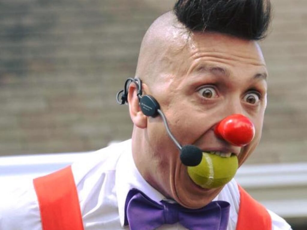 Clown avec micro à l'oreille et une balle de tennis dans la bouche